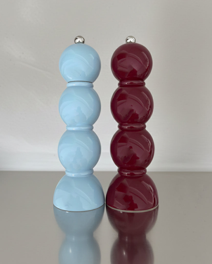 Two marbled salt and pepper shakers, one blue and one red, on a reflective surface with a neutral background.