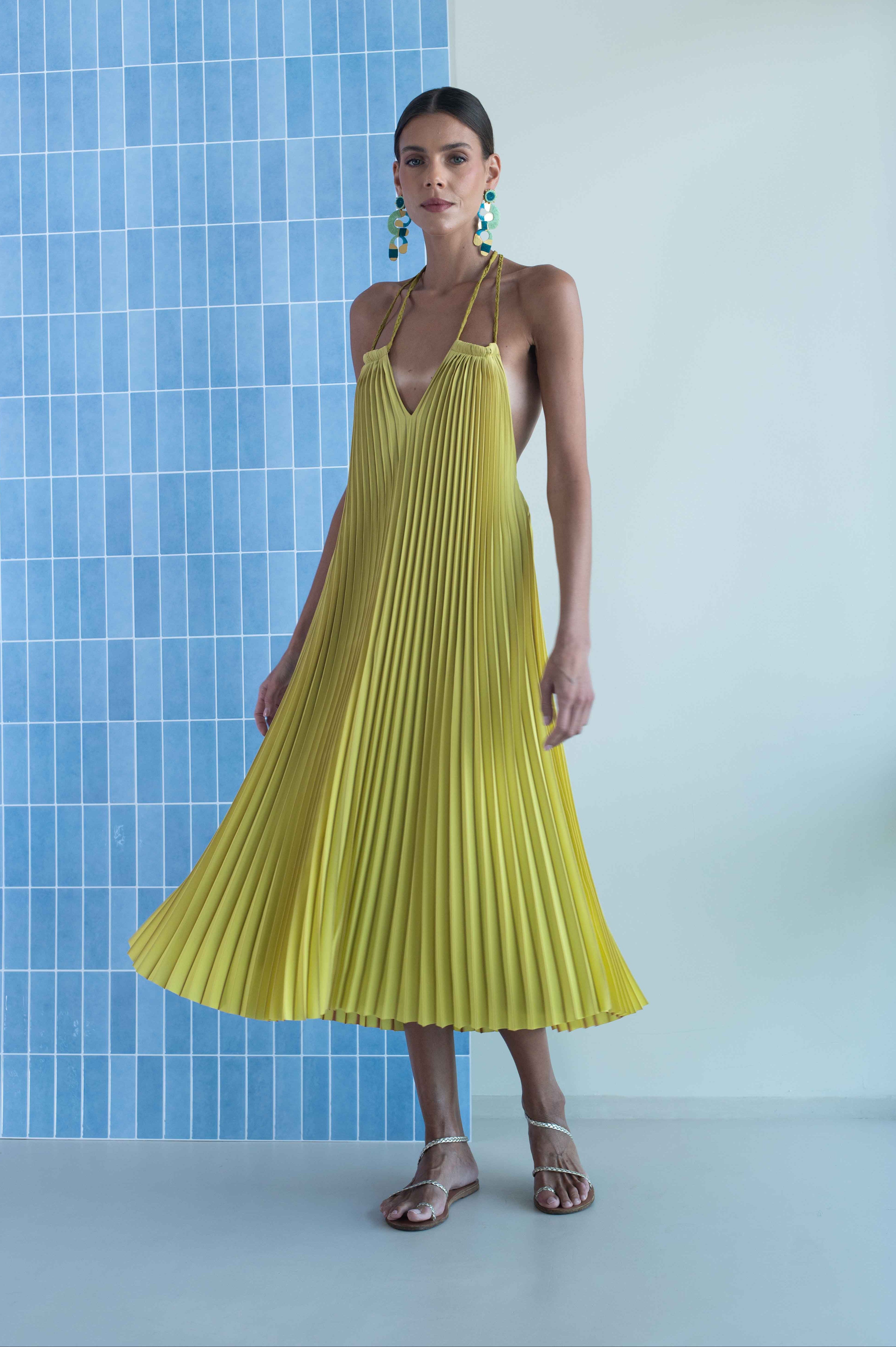 Woman wearing a yellow pleated dress against a blue tiled wall.